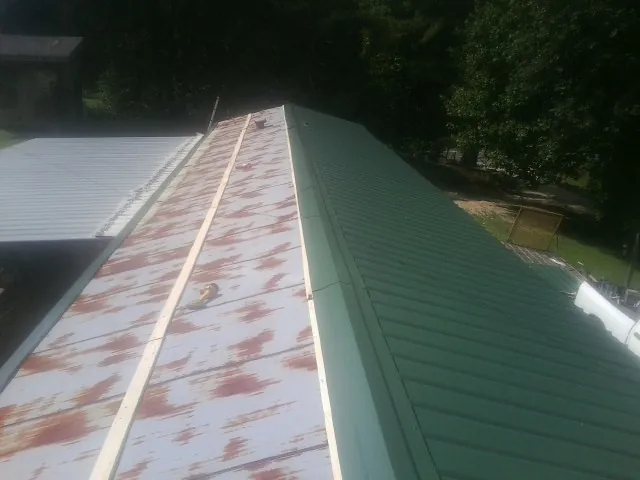 Old rusted panels beside newly installed green metal roofing in Trinity