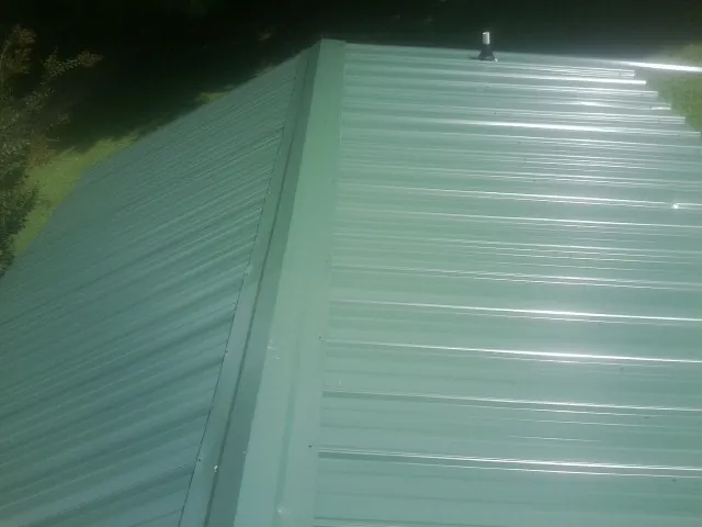 New green metal panels meeting at the ridge of a roof — Flat Roof Repair work by our crew in Trinity