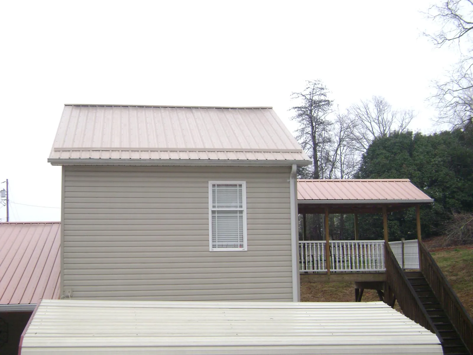 Tan metal roofs on a two story addition and attached porch, from a Roof Replacement job in Trinity